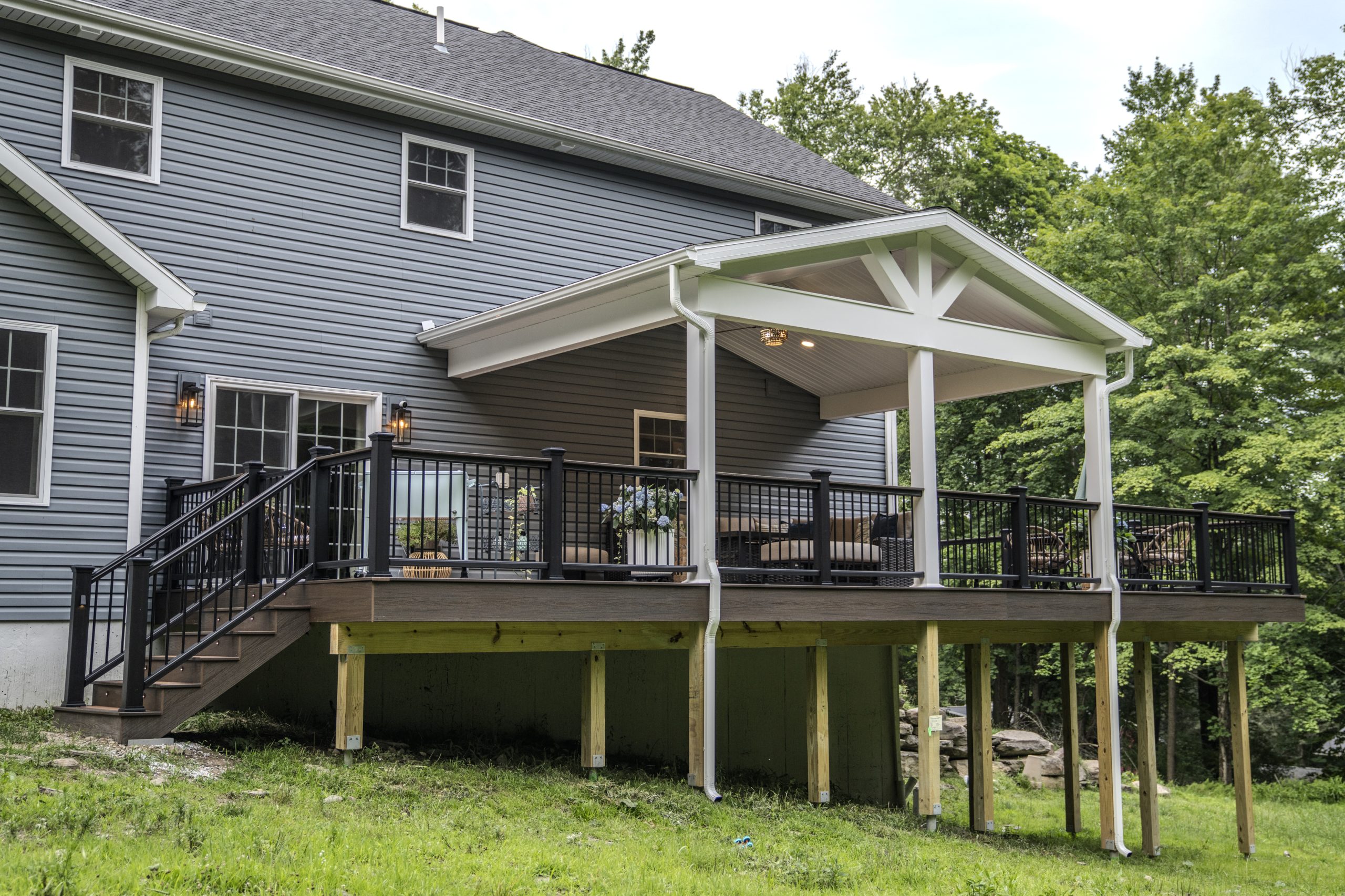 Exterior wide shot of a completed elevated deck project in Clark's Summit, showing the white gable roof extension, composite decking, and sturdy support posts.