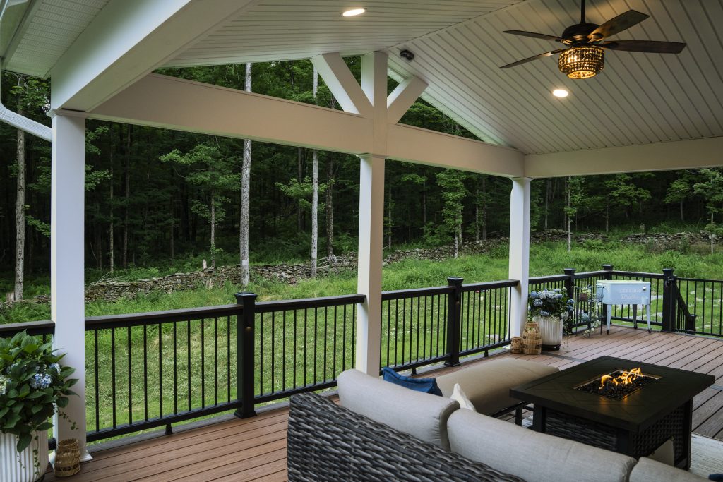View looking out from a covered porch, highlighting the custom white timber framing, vaulted ceiling, and recessed lighting against a green landscape.