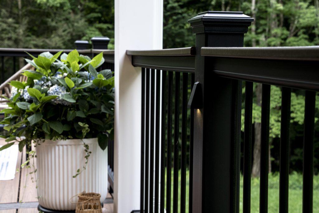 Focused detail of a downward-facing LED accent light mounted on a black aluminum railing post for evening ambiance and safety.
