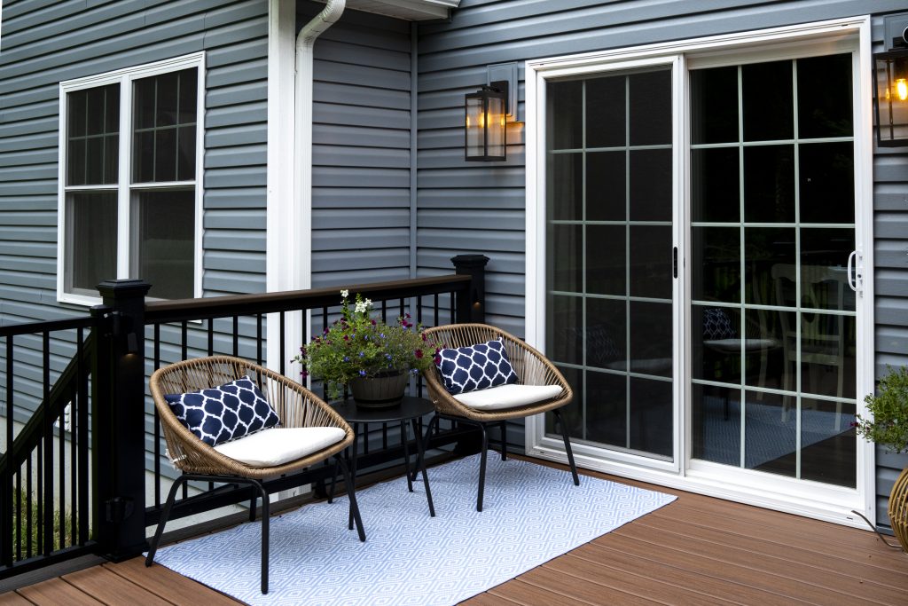 Small sitting area with two modern wicker chairs and a blue rug placed next to the sliding glass patio doors on a newly constructed deck.