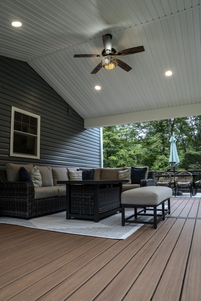 Relaxing covered porch atmosphere featuring a lit fire pit table, ceiling fan, and comfortable outdoor furniture protected by a weather-resistant roof.