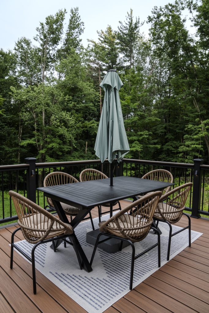 Modern outdoor dining set with wicker chairs and a closed umbrella centered on a maintenance-free composite deck surface.