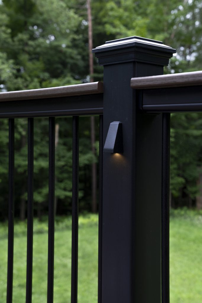Focused detail of a downward-facing LED accent light mounted on a black aluminum railing post for evening ambiance and safety.