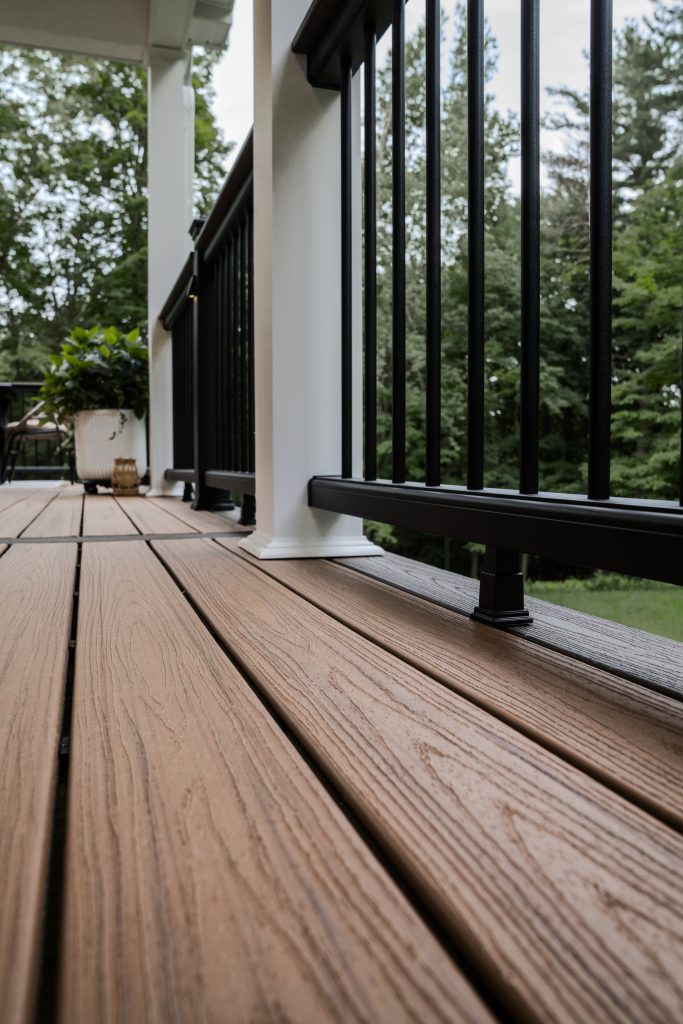 Low-angle close-up emphasizing the wood-grain texture of the composite flooring and the profile of the "cocktail rail" railing design.