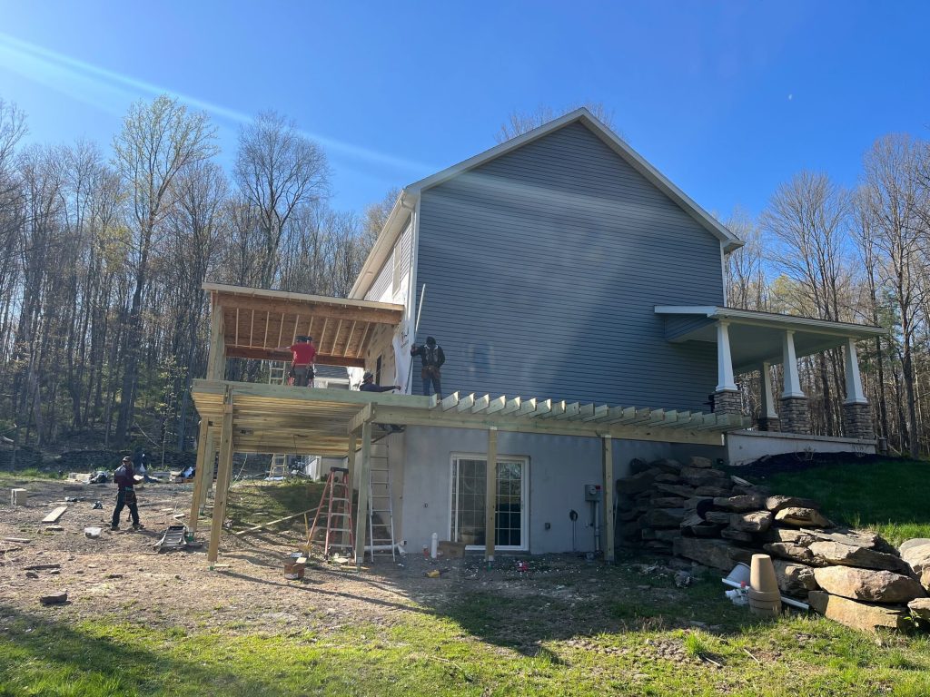 Construction in progress of a custom elevated deck and covered porch addition on a two-story gray home in Clark's Summit, PA.