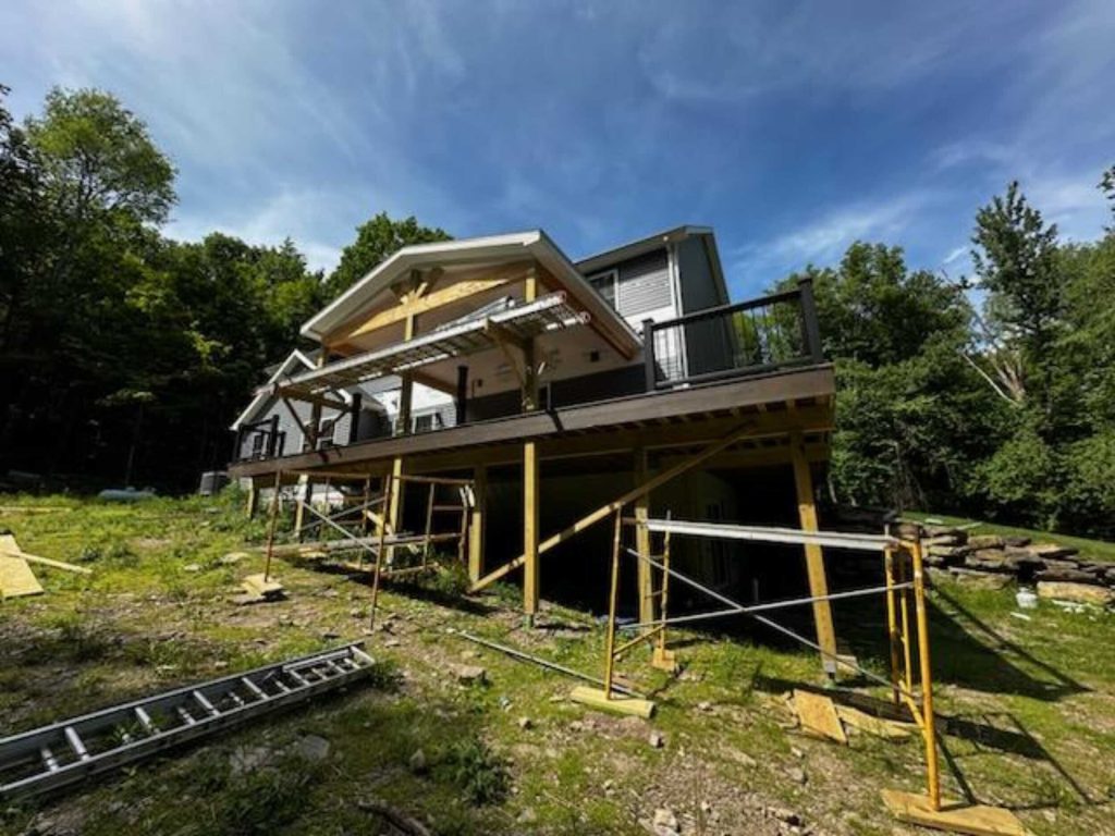 View from the backyard of a nearly completed large composite deck featuring black aluminum railings and a vaulted covered roof section.