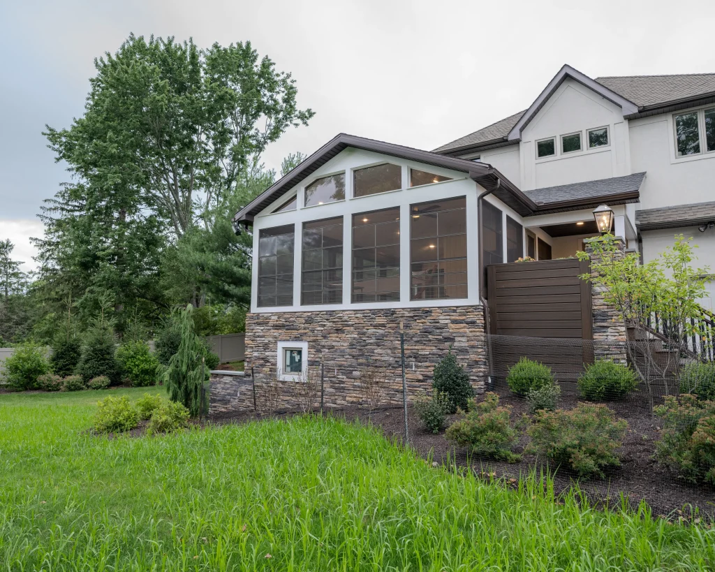 Exterior view of a custom three-season outdoor living space with Eze-Breeze windows, cultured stone veneer, and premium finishes in Dalton, PA.